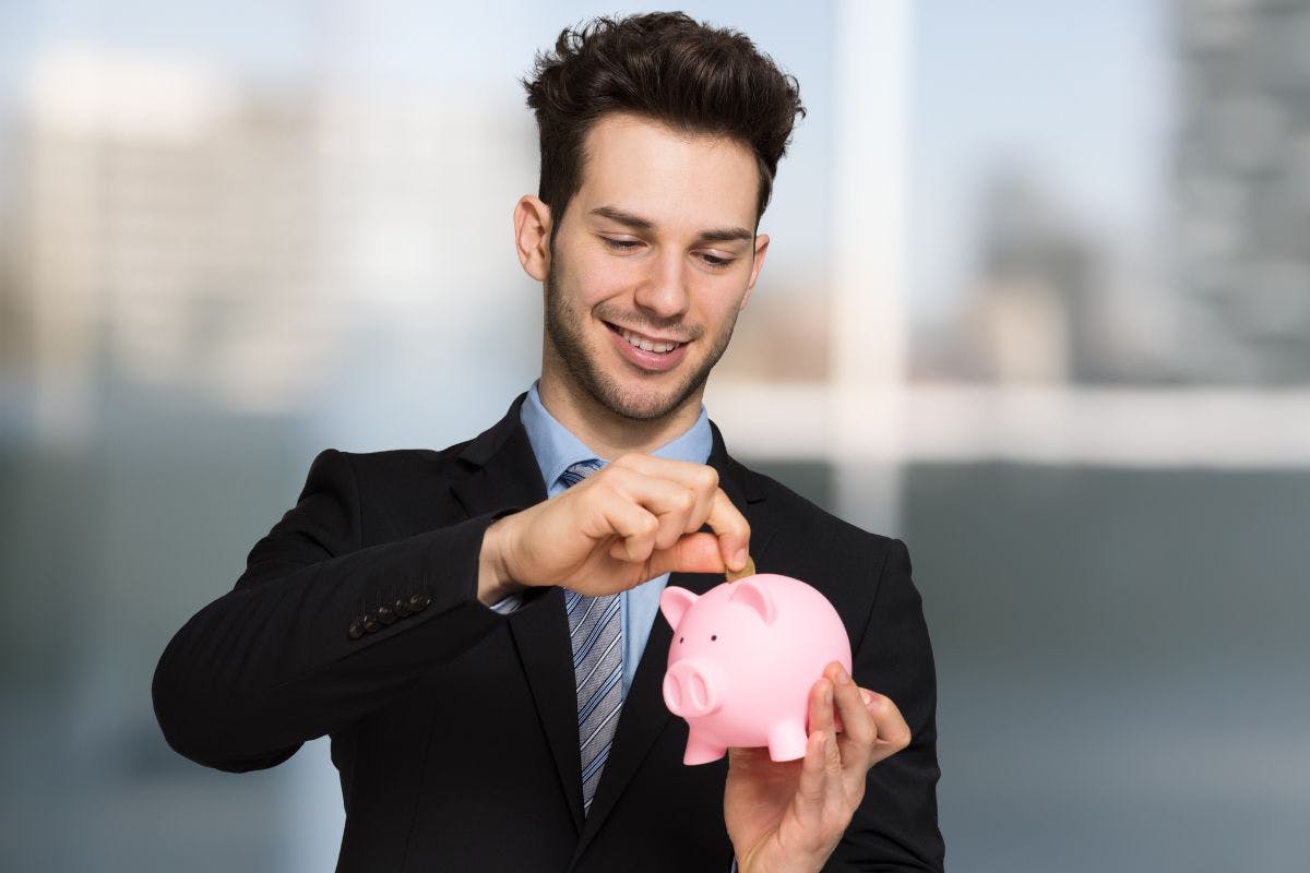 Jeune homme en complet qui met une pièce de monnaie dans un cochon rose